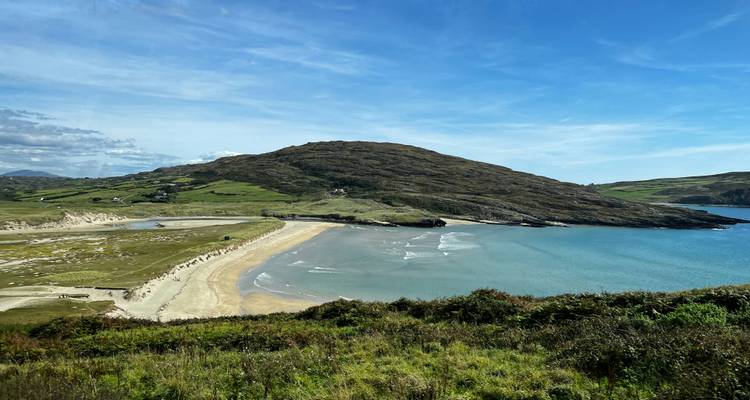 Ein sandiger Strand mit sanften Wellen und grasbewachsenen Hügeln.