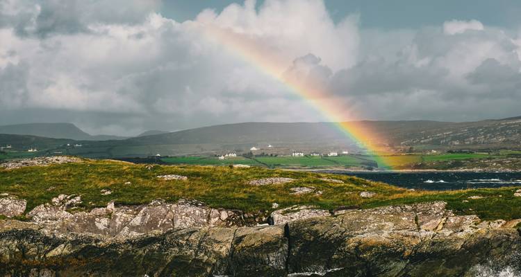 Ein leuchtender Regenbogen über ländlichen Feldern und Hügeln.