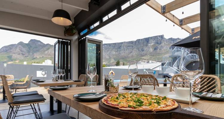 Außenbereich eines Restaurants mit Bergblick und Pizza auf einem Tisch.