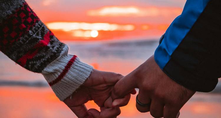 Close-up of two people holding hands at sunset.