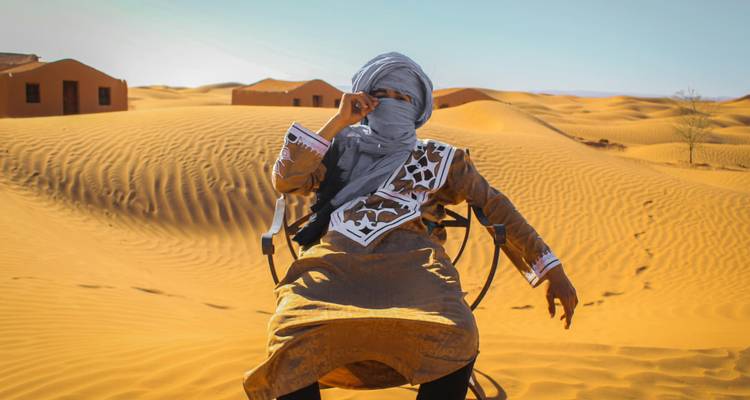 Person in traditional attire sitting in desert.