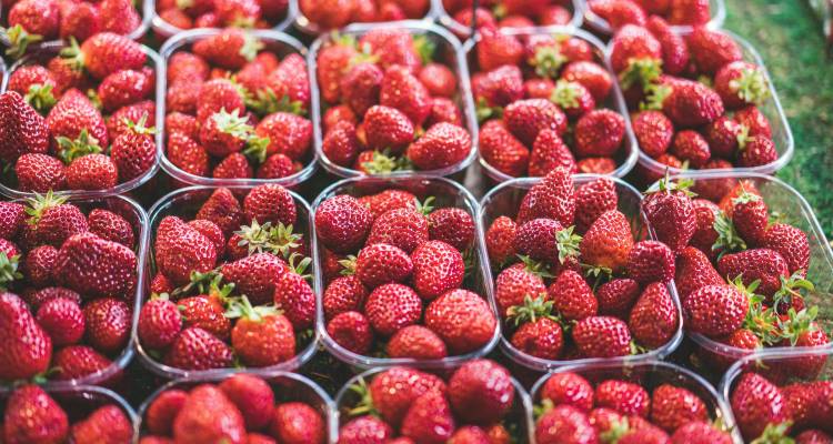 Close-up beeld van meerdere plastic bakjes gevuld met verse rijpe aardbeien uitgestald op een marktkraam