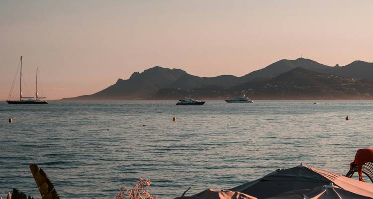 Rustige Mediterrane baai met zeilboten en verre bergsilhouet gebaad in warm avondlicht