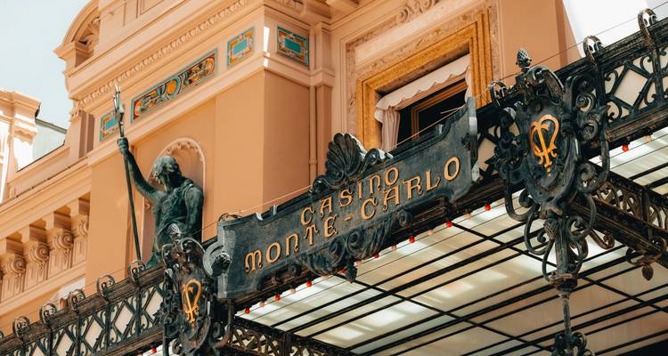 Elegante ingangsluifel van ijzer en glas van het beroemde Casino de Monte-Carlo met sierlijke bewegwijzering en standbeeld