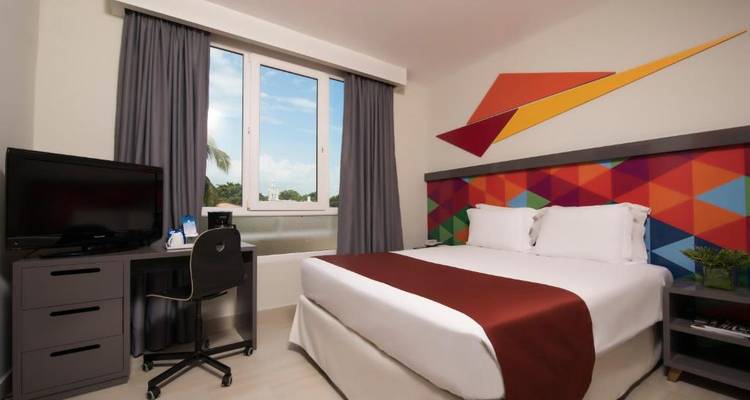 A hotel room featuring a bed, desk, and window view.