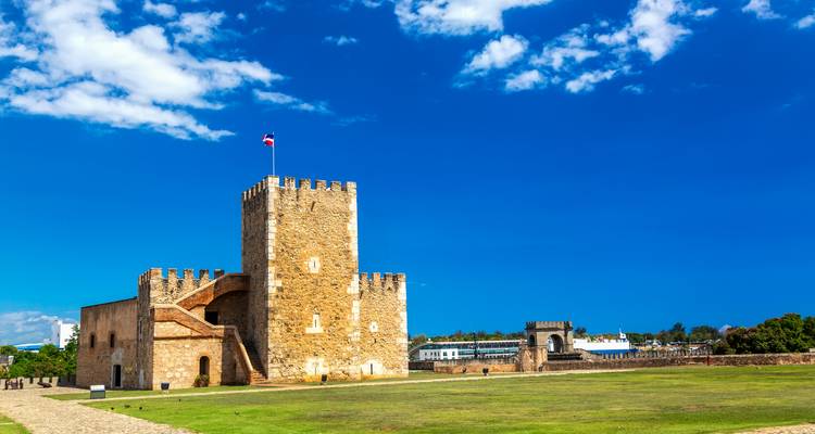 Une forteresse historique sous un ciel bleu dégagé, avec une tour en pierre et des remparts.