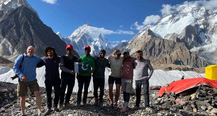 Un grupo de excursionistas parados con una bandera frente a montañas cubiertas de nieve.