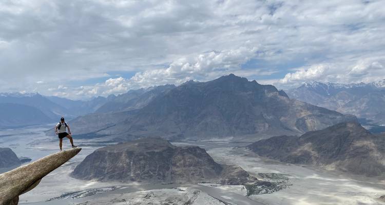 Una persona parada en el borde de un acantilado de montaña con un vasto paisaje abajo.