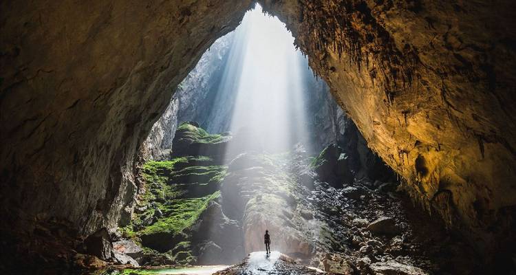Lumière du soleil pénétrant dans une grande grotte avec une minuscule silhouette.