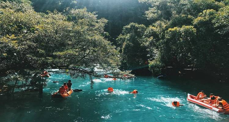 Des gens portant des gilets de sauvetage nageant et faisant du kayak dans une eau bleue claire entourée d'une végétation luxuriante.
