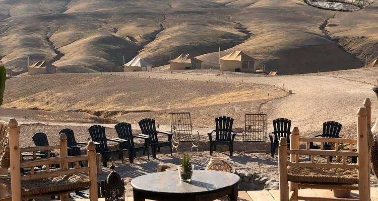 Desert camp with chairs and tents, surrounded by barren hills.