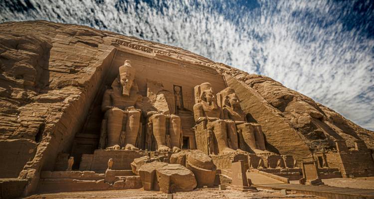 Le Grand Temple d'Abou Simbel avec de grandes statues sculptées dans la roche sous un ciel dramatique.