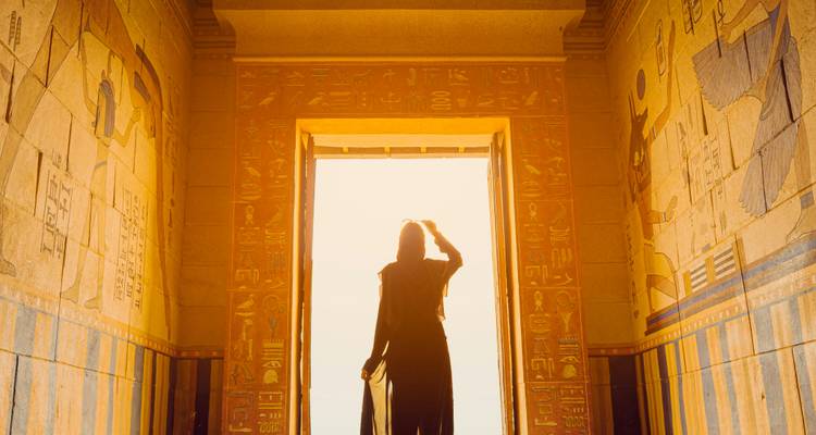 Silhouette d'une personne debout dans un temple égyptien richement décoré avec la lumière du soleil qui pénètre par l'entrée.