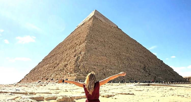 Femme aux bras étendus devant une grande pyramide.
