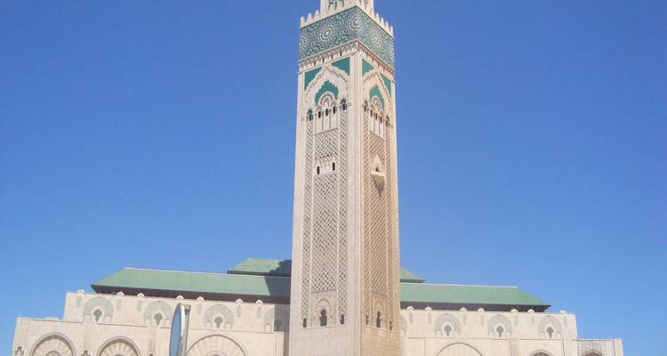 Une grande mosquée aux motifs complexes et un haut minaret sous un ciel bleu dégagé.