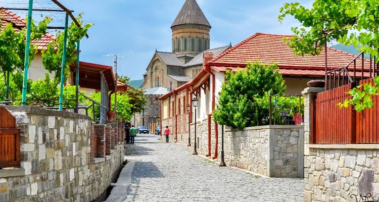 A cobblestone street lined with stone and brick houses, leading to a large cathedral or church.