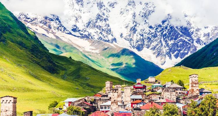 A picturesque village with stone towers nestled in a valley with snowy mountains.