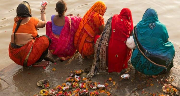 Femmes en saris colorés accomplissant des rituels au bord d'une rivière.