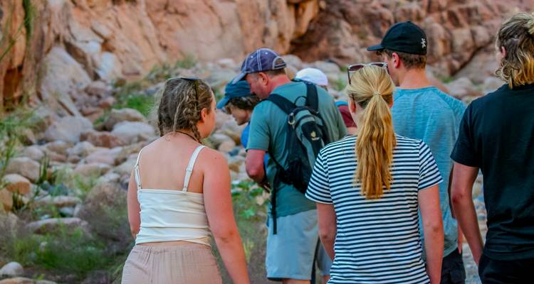 Gruppe junger Reisender beim Wandern durch einen felsigen Canyon mit warm gefärbten Sandsteinwänden.
