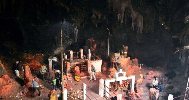 Personas dentro de una cueva con estatuas religiosas y ofrendas.