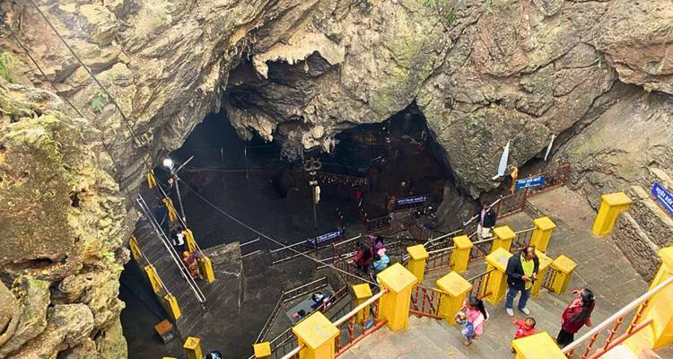 Imagen de la entrada de una cueva natural con personas y barandilla amarilla.