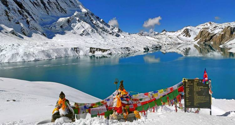 Lac immaculé entouré de montagnes enneigées et de drapeaux de prières colorés.