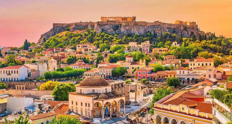Cálida luz del atardecer sobre los coloridos tejados de Atenas con la Acrópolis prominente en el afloramiento rocoso.