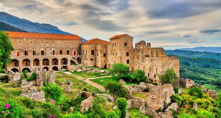 Ruinas bien conservadas de un monasterio medieval situadas entre exuberantes colinas verdes con un cielo dramático en lo alto.