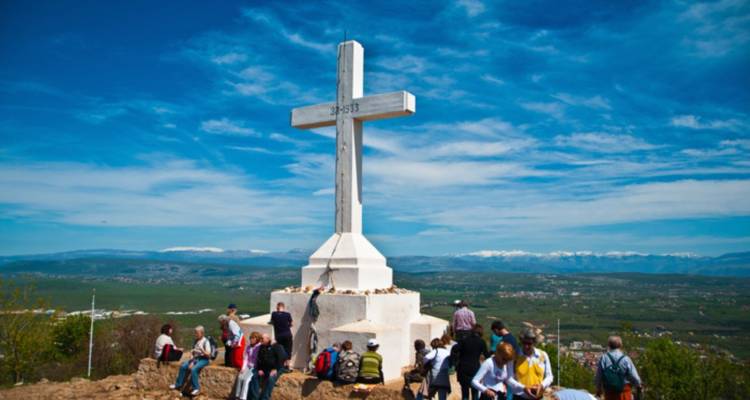 Grupo de personas cerca de una gran cruz blanca en una colina.