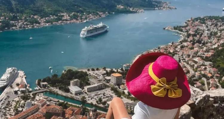 Person mit Hut blickt über eine Bucht mit einem Kreuzfahrtschiff.