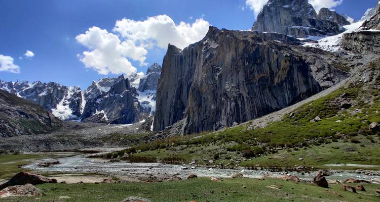 Agujas de granito escarpadas y parches de nieve que se elevan sobre una pradera alpina cubierta de hierba y un arroyo