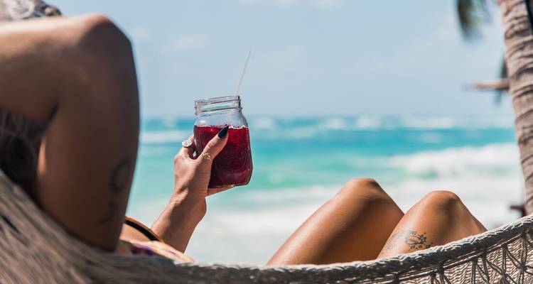 Une personne se détendant dans un hamac près d'une plage avec une boisson.