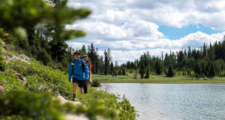 Excursionistas caminando junto a un lago sereno rodeado de árboles.