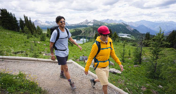 Dos excursionistas sonriendo con un lago y montañas de fondo.