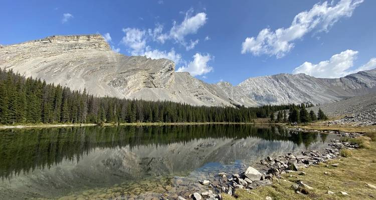 Lago tranquilo con reflejo de montañas rocosas en un día despejado.
