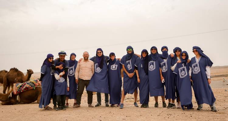 Groep toeristen gekleed in blauwe traditionele gewaden poserend met kamelen in woestijnkamp