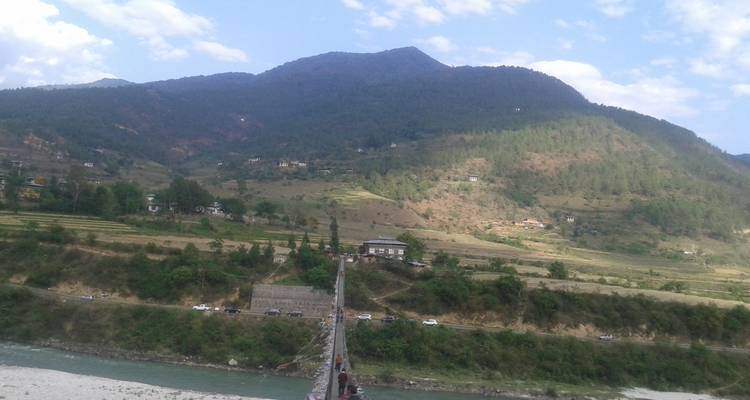 Un puente colgante sobre un río con montañas en el fondo.
