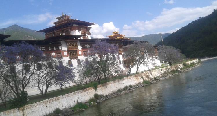 Una estructura tradicional butanesa similar a una fortaleza con un río al frente y montañas detrás.