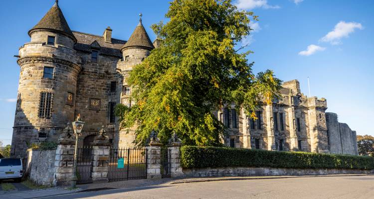 Palais historique de Falkland avec des arbres et un ciel lumineux.