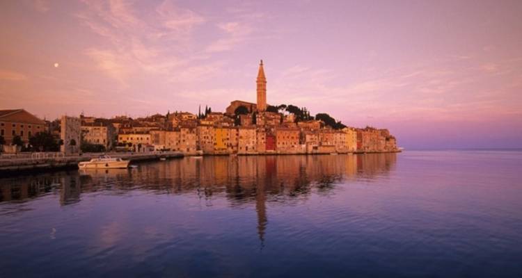 Rovinj al atardecer con la torre de la iglesia contra un cielo rosado.