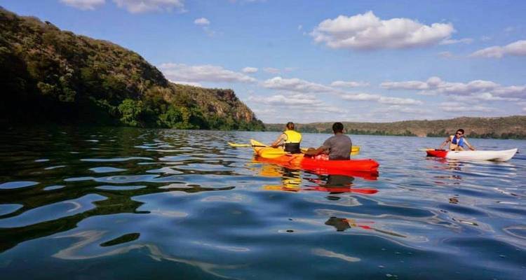 Kayakistes pagayant sur un lac bleu calme entouré de collines boisées et de nuages épars