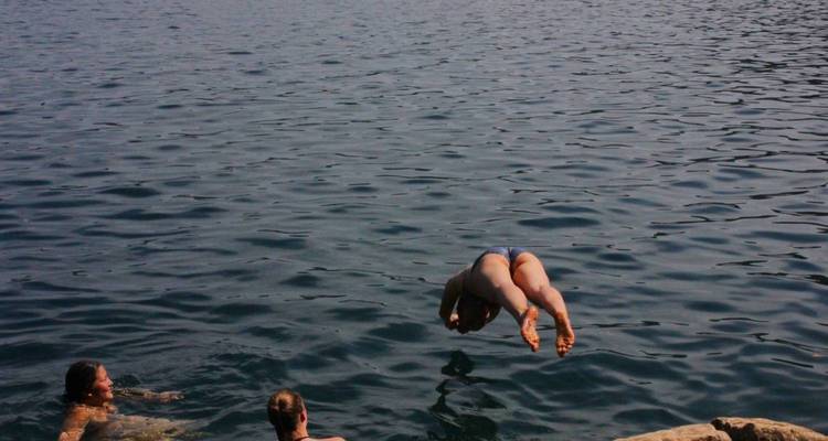 Personne en plein plongeon dans un lac bleu profond tandis que des amis observent depuis l'eau