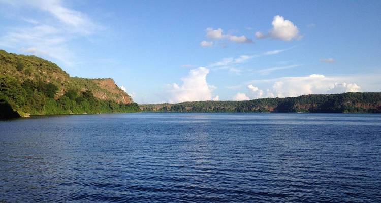 Vaste lac tranquille encadré par des collines vertes et un ciel bleu parsemé de nuages épars