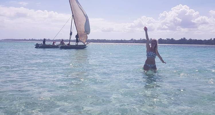 Une femme dans la mer avec un voilier à proximité dans des eaux claires.