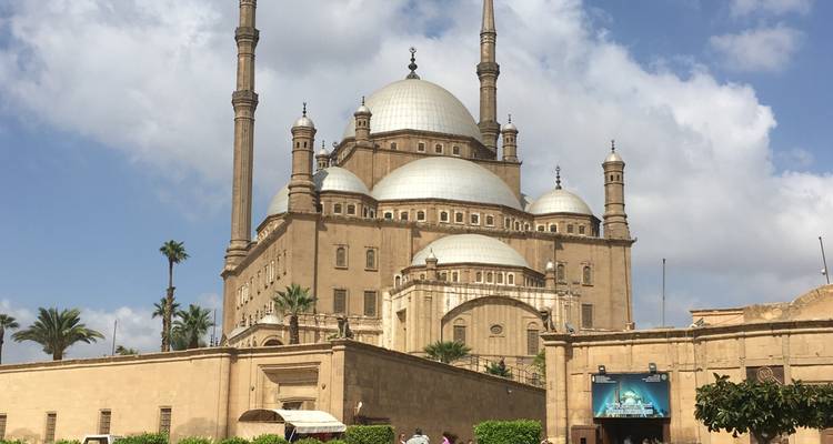 Mosquée avec de nombreux dômes et minarets, ciel dégagé et quelques personnes.