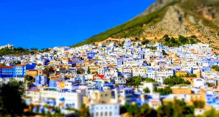 Un paysage urbain à flanc de colline avec des bâtiments bleus et blancs et des montagnes au loin.