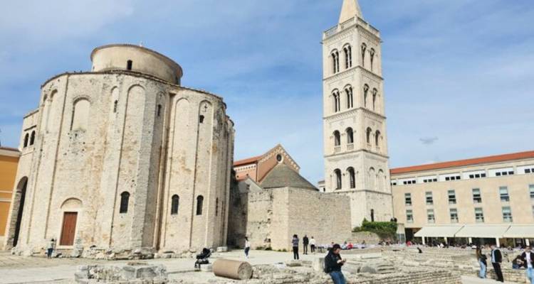 Kerk en klokkentoren met mensen eromheen op een heldere dag.