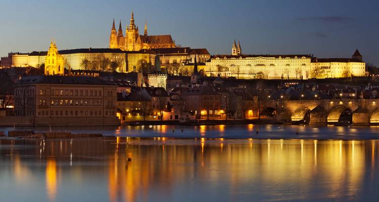 Vista de un castillo iluminado y río durante el anochecer.