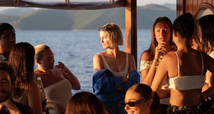 Grupo de personas socializando en un barco con vista a las montañas y el mar.
