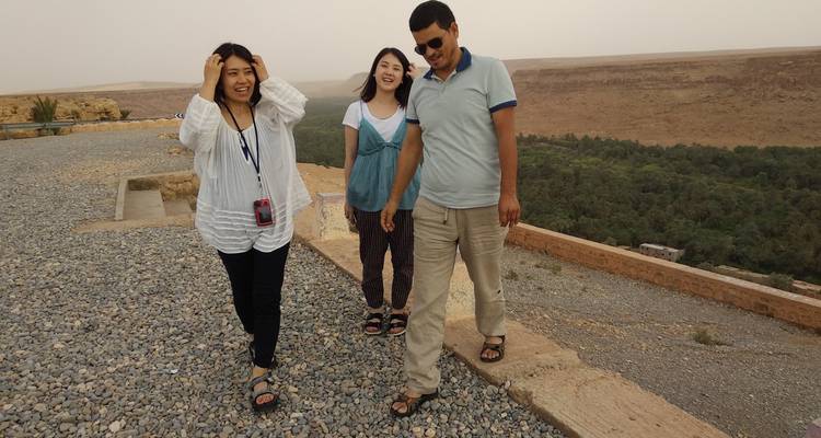 Grupo de tres viajeros caminando en un mirador de grava sobre un valle de oasis desértico.
